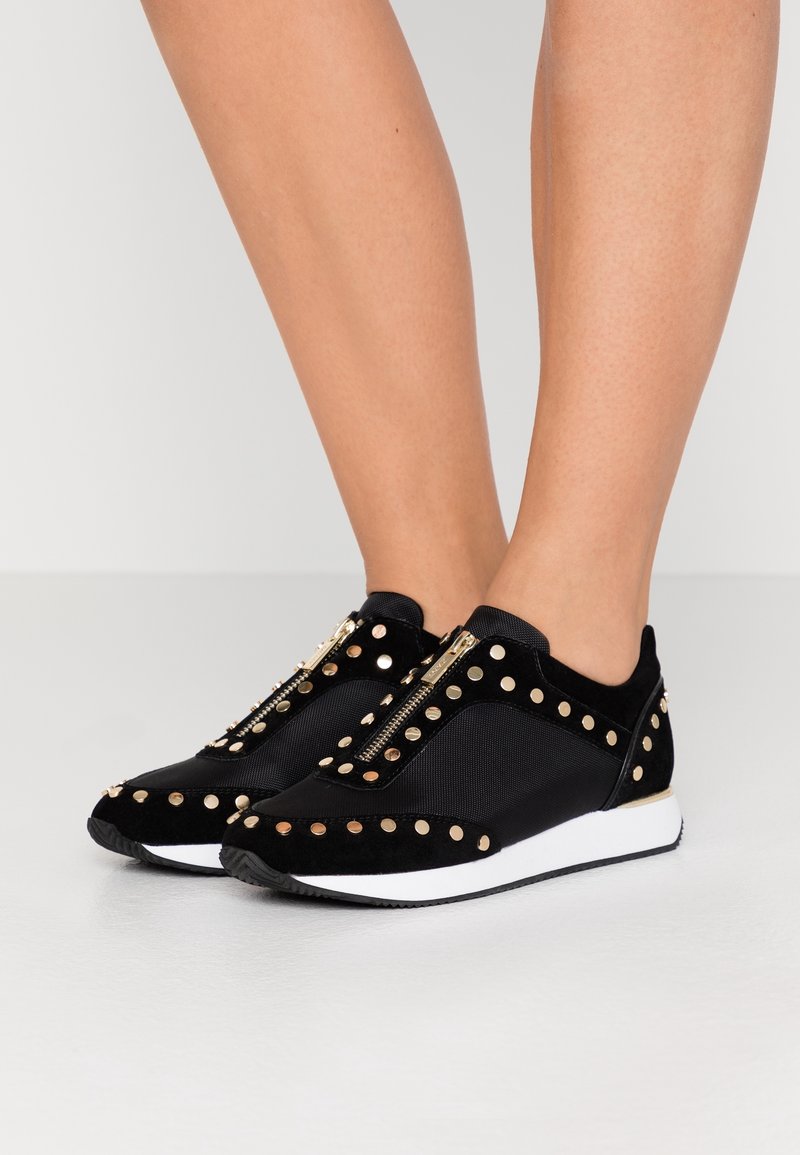 Svarta sneakers i mocka och mesh har guldnitar och dragkedjestängning, med en vit vadderad sula och rundad tådesign.