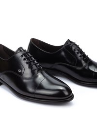 Zapatos de vestir de cuero negro con una textura suave, punta afilada y seis pares de ojales para cordones. Diseño notable de cap-toe.