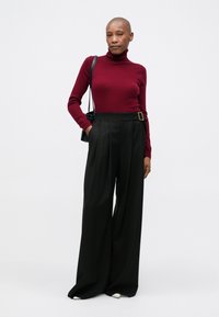 Burgundy garbó pulóver, magas derekú fekete, széles lábú nadrággal, amely övcsattal, sima anyaggal és oldalsó zsebekkel rendelkezik.