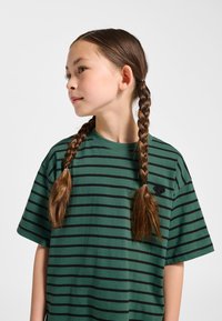 Grön bomullst-shirt med svarta horisontella ränder, korta ärmar och rund halsringning. Har en liten broderad logotyp på bröstet.