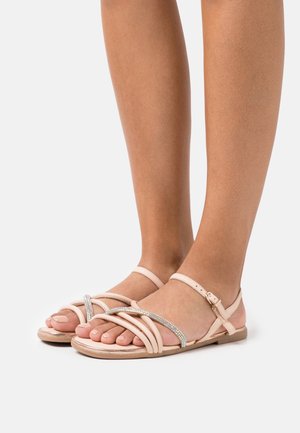 Sandales rose clair avec plusieurs brides croisées et un accent décoratif en strass. Semelle plate et bride de cheville réglable.