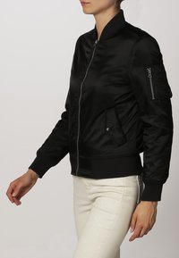 Giacca bomber in satin nero con zip frontale, polsini a coste e tasca laterale. Caratterizzata da una silhouette classica e una finitura elegante.
