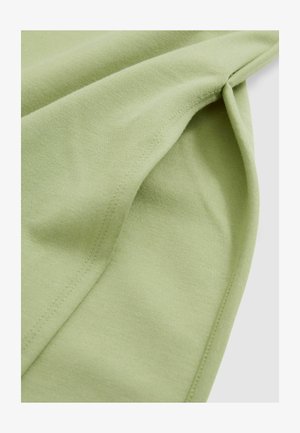 Tejido verde claro con una textura suave, con costuras visibles y pliegues caídos, que muestran su calidad ligera y transpirable.