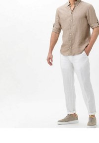 Camisa de lino marrón claro, con mangas enrolladas y botonada en la parte delantera; combinada con pantalones de lino blanco de corte holgado; zapatillas deportivas grises con detalles texturizados.