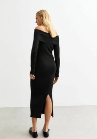 Svart ribbad off-shoulder klänning med långa ärmar, en högt skuren sidoklippning och en figurnära silhuett. Slät textur och ankellång design.