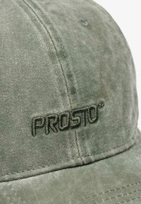 Zielona materiałowa czapka z lekko fakturowaną powierzchnią. Na przednim panelu znajduje się haftowane logo "PROSTO" w tym samym odcieniu zieleni.