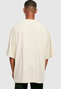 Overdimensioneret beige t-shirt med rund hals og korte ærmer. Fremstillet af blød bomuld, med et rent design uden synlige mønstre eller accenter.