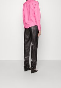 Camicia button-up rosa con maniche lunghe, abbinata a pantaloni di pelle nera e scarpe con tacco alto dotate di un design ritagliato unico.