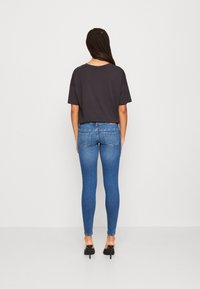 Top negro de manga corta combinado con jeans de denim azul ajustados, con bolsillos, y llevado con zapatos de tacón. La textura parece suave.