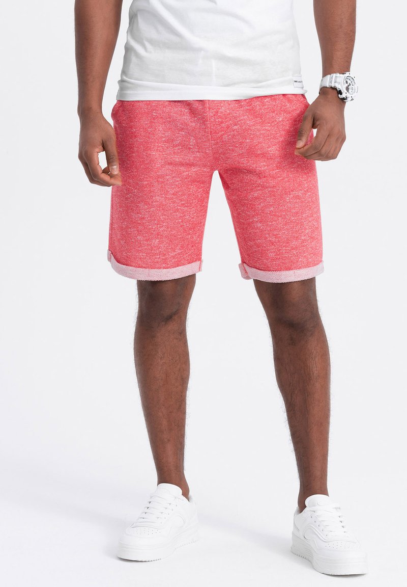 Shorts rouge chinés avec des ourlets retroussés, fabriqués dans un tissu mélangé. Associés à des baskets blanches, mettant en valeur une coupe décontractée.