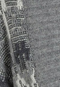 Szary dzianinowy tekstylia z mieszanką wzorów; cechuje się różnorodnymi fakturami i frędzlami na krawędzi w jasnych i ciemnych odcieniach szarości.