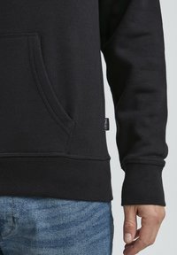 Il hoodie nero presenta una tasca frontale, polsini a coste e un orlo dritto. Realizzato in materiale morbido con dettagli di cucitura visibili.