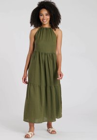 Maxi-jurk in olijfgroen, gemaakt van textuurstof met een halternek, geplooide borst en gelaagde rok. Gepaard met neutrale sandalen.