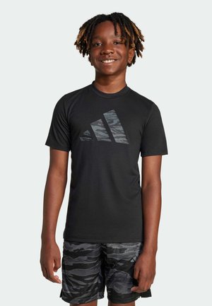 Maglietta nera a maniche corte con il logo Adidas in camuffamento sul davanti, abbinata a pantaloni corti grigi in camuffamento con un motivo simile.