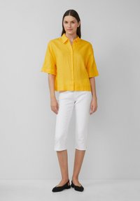 Chemise en lin jaune à manches courtes avec un devant boutonné, associée à un pantalon blanc court et des chaussures plates noires. Design simple et décontracté.