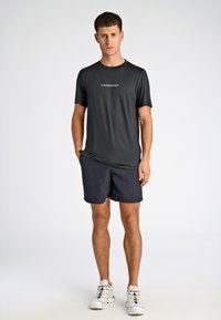Svart t-shirt med kort ärm och texten "LINDBERGH", i kombination med marinblå shorts. Modellen har på sig vita sportskor med flerfärgade snören.