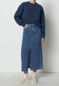 Sudadera azul marino de manga larga combinada con una falda de mezclilla de cintura alta que presenta una abertura frontal. Sandalias beiges ligeras completan el conjunto.