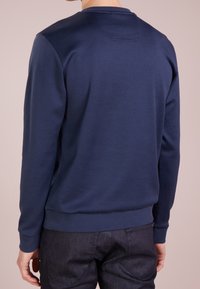 Marinblå sweatshirt med långa ärmar, ribbade muddar och nederkant. Slät textur, minimala sömmar, med en liten detalj vid nacklinjen bak.