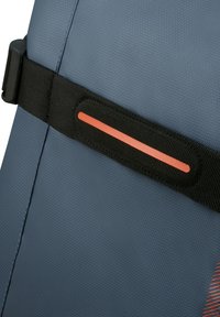 Blue fabric seat with a textured surface, featuring a black strap and a thin orange accent. Focus on utility and secure attachment.