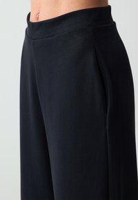 Zwarte wijde pantalons van een zachte, lichte stof met een hoge tailleband en zijzakken voor gemak.