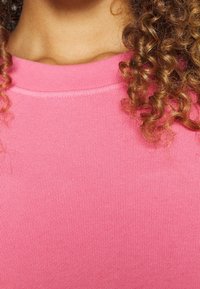 Rosa ribbad stickad topp med rundad halsringning och strukturerad tyg. Designen är figursydd och slät, utan synliga dekorationer.
