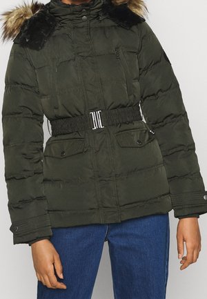 Giacca puffer verde scuro con cappuccio in pelliccia, vita con cintura, tasche con zip e bottoni, indossata con jeans blu da un modello su uno sfondo neutro.