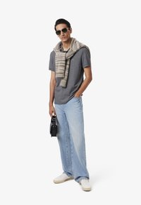 Grå pikétröja med en liten logo, ljusblå jeans, vita sneakers och en randig beige scarf över axlarna. Svart väska.