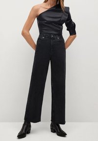 Top negro de un solo hombro en material suave, combinado con vaqueros negros de tiro alto y pierna ancha, con bajos sin rematar y un sutil desgaste.