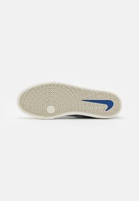 White sneaker sole with a patterned grip, featuring a blue Nike logo, and a zigzag texture across the rubber surface.