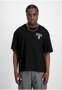 T-shirt noir à manches courtes avec le texte blanc "BERLIN ALLEMAGNE" et un graphique de ballon sur la poitrine gauche. Coupe ample, en coton, design sobre.