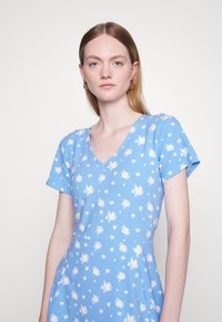 Vestido floral azul claro com decote em V e mangas curtas. Apresenta padrões de flores brancas espalhadas em um tecido liso e macio.