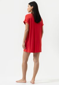 Pigiamino rosso a maniche corte realizzato in morbido tessuto, con una vestibilità rilassata e un colletto rotondo, dalla texture liscia e con lunghezza sopra al ginocchio.