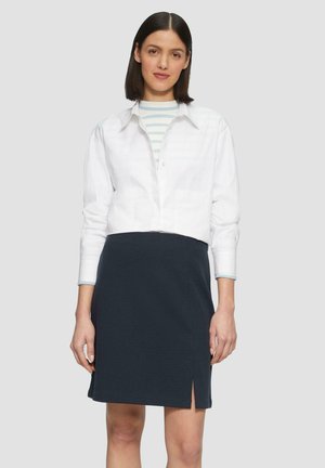 Witte cropped button-up shirt over een lichtblauw en wit gestreept langemouwen shirt, gecombineerd met een donker navy knielange rok met een zijsplit.