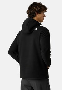 Czarny polarowy hoodie z kapturem i długimi rękawami. Posiada małe białe logo na plecach przy ramieniu. Gładka tekstura, luźny krój.