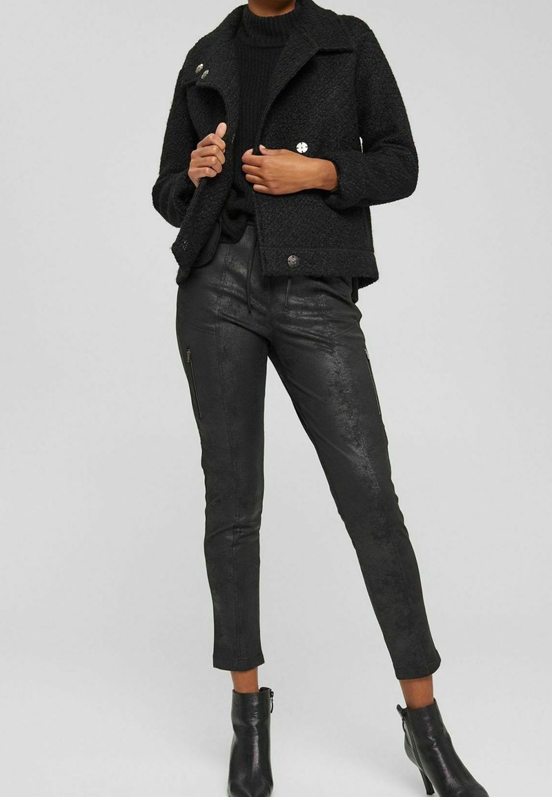 Black textured jacket with button closure, paired with fitted black leather pants featuring zip accents and ankle boots, all in dark hues.