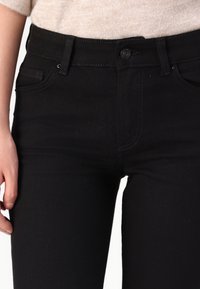Les jeans en denim noir présentent une taille mi-haute, un design classique à cinq poches et une coupe slim. Le tissu a une texture lisse avec des détails de couture minimaux.