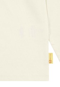 Camicia a maniche lunghe di colore crema chiaro realizzata in cotone. Presenta un'etichetta con sfondo giallo e una texture liscia e uniforme. Nessun motivo visibile.
