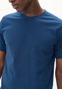 Mėlyna trumpomis rankovėmis T-shirt, pagaminta iš minkštos tekstūruotos medžiagos, su apvalia kaklo iškirpte, turinti švelnų heather raštą ir laisvą siluetą.