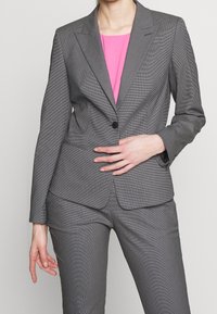 Costume gris sur mesure avec un motif texturé. Comprend un blazer à bouton unique et un pantalon slim, accompagné d'un haut rose vif.