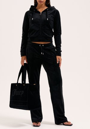 Tuta in velluto nero con una felpa corta con zip e pantaloni con cordino. I dettagli notevoli includono una grande borsa tote nera con un accento dorato e logo.