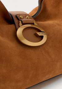 Brown suede handbag with a gold circular hardware accent featuring a "G" logo. The bag has a soft texture and a structured shape.