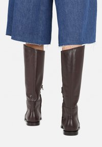 Brown leather knee-high boots with a smooth texture, featuring a side zipper and a low heel, paired with blue denim culottes.
