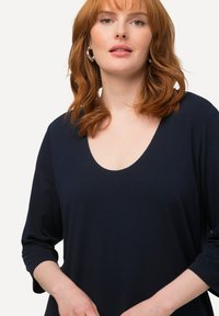 Navyblaues Oberteil mit Rundhalsausschnitt und Dreiviertelärmeln, hergestellt aus einem weichen Stoff. Verfügt über eine glatte Textur und minimale Details.