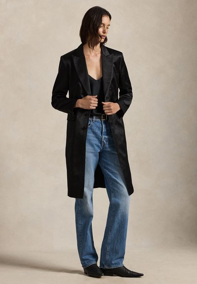 Casaco longo de cetim preto com colarinho xale, combinado com um top preto e jeans de perna direita azul claro; usado com botas pretas pontiagudas.