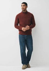 Maglione lavorato a maglia color marrone scuro con motivo testurizzato, colletto e polsini a coste, abbinato a jeans blu e scarpe in suede marrone chiaro.