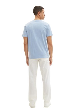 Hellblaues Baumwoll-T-Shirt mit kurzen Ärmeln, rundem Ausschnitt und komfortablem Schnitt, kombiniert mit weißen Hosen und Sneakers.