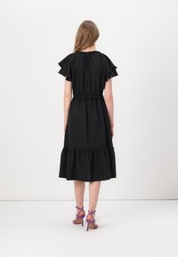 Black cotton dress with flutter sleeves, gathered waist, and a tiered skirt. Worn with strappy purple heels.