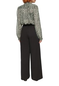 Doorzichtig groene blouse met een textuurpatroon, gecombineerd met zwart-witte hoge taille broek met wijde pijpen. Beide hebben een losse pasvorm en een vloeiende silhoët.