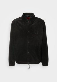 Zwart corduroy jasje met knoopsluiting, geborduurd logo, puntkraag, zijzakken en een verstelbare koord aan de onderkant.