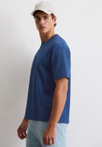 Granatowa bawełniana koszulka z okrągłym dekoltem i krótkimi rękawami, o prostym kroju i minimalistycznym wzornictwie, w zestawie z jasnoniebieskimi dżinsami.